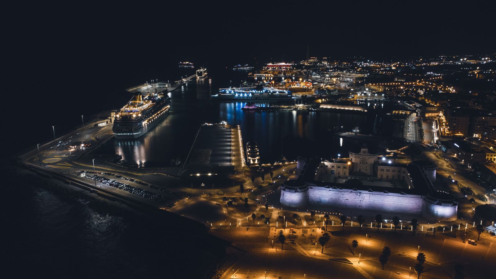 Aerial night view of a harbor with a lit cruise ship at the pier, the kind of scene behind daily cruise industry news