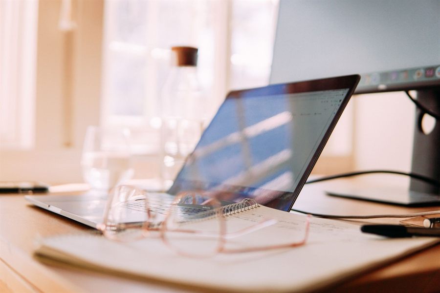 Laptop on a sunny desk with glasses and a notebook