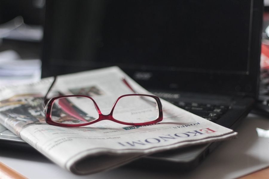 Red glasses resting on a newspaper beside a laptop